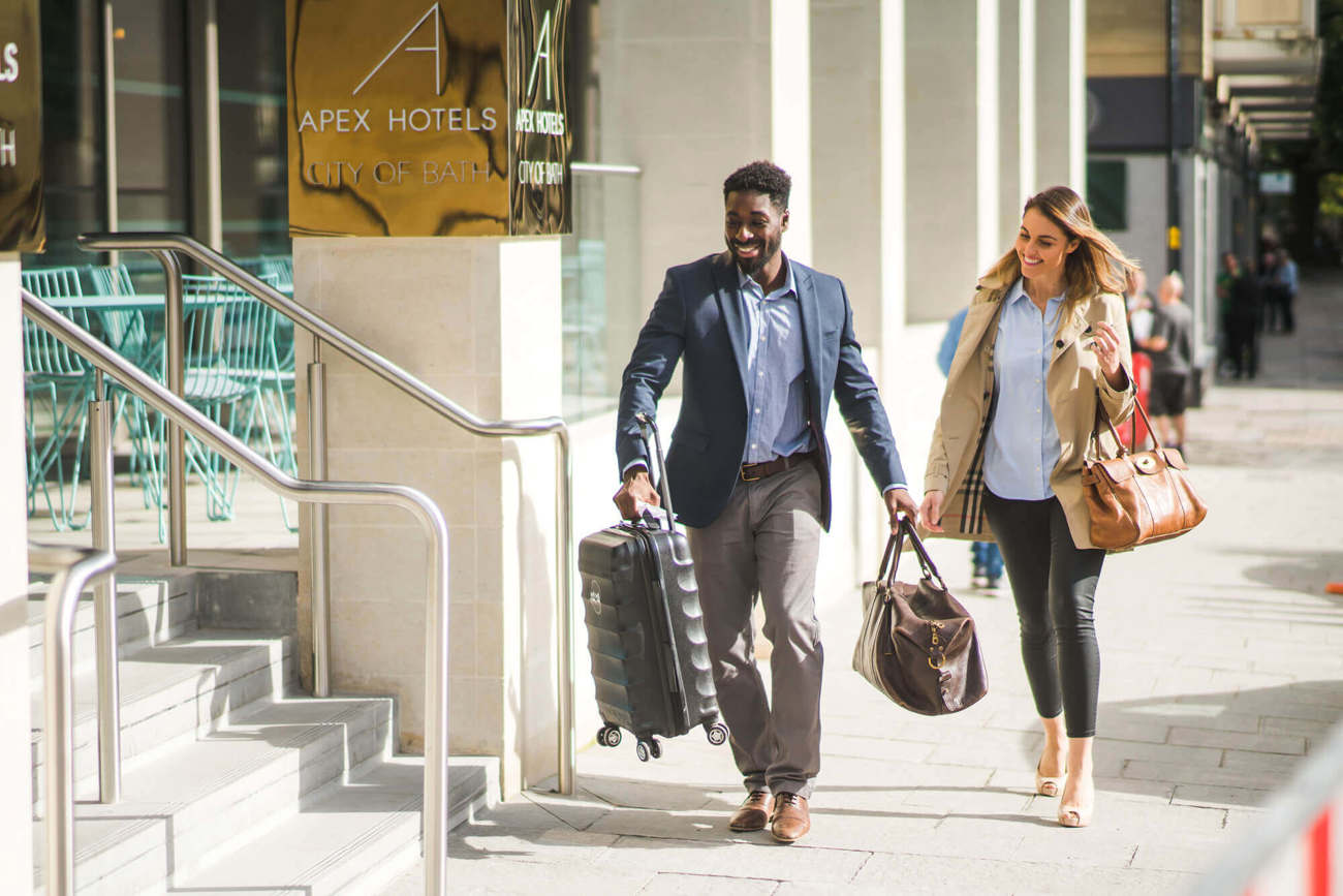 Female guest being lead into the hotel by male employee helping her with her bags